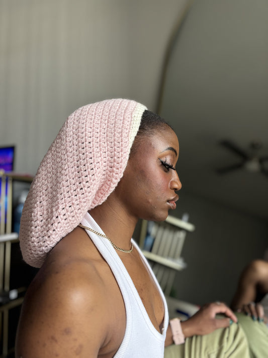 Woman wearing a pink crochet locsoc hat in an indoor setting