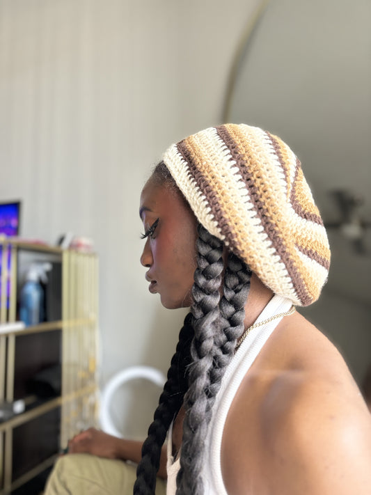 Person wearing a striped crochet beret with braided hair in a room setting.