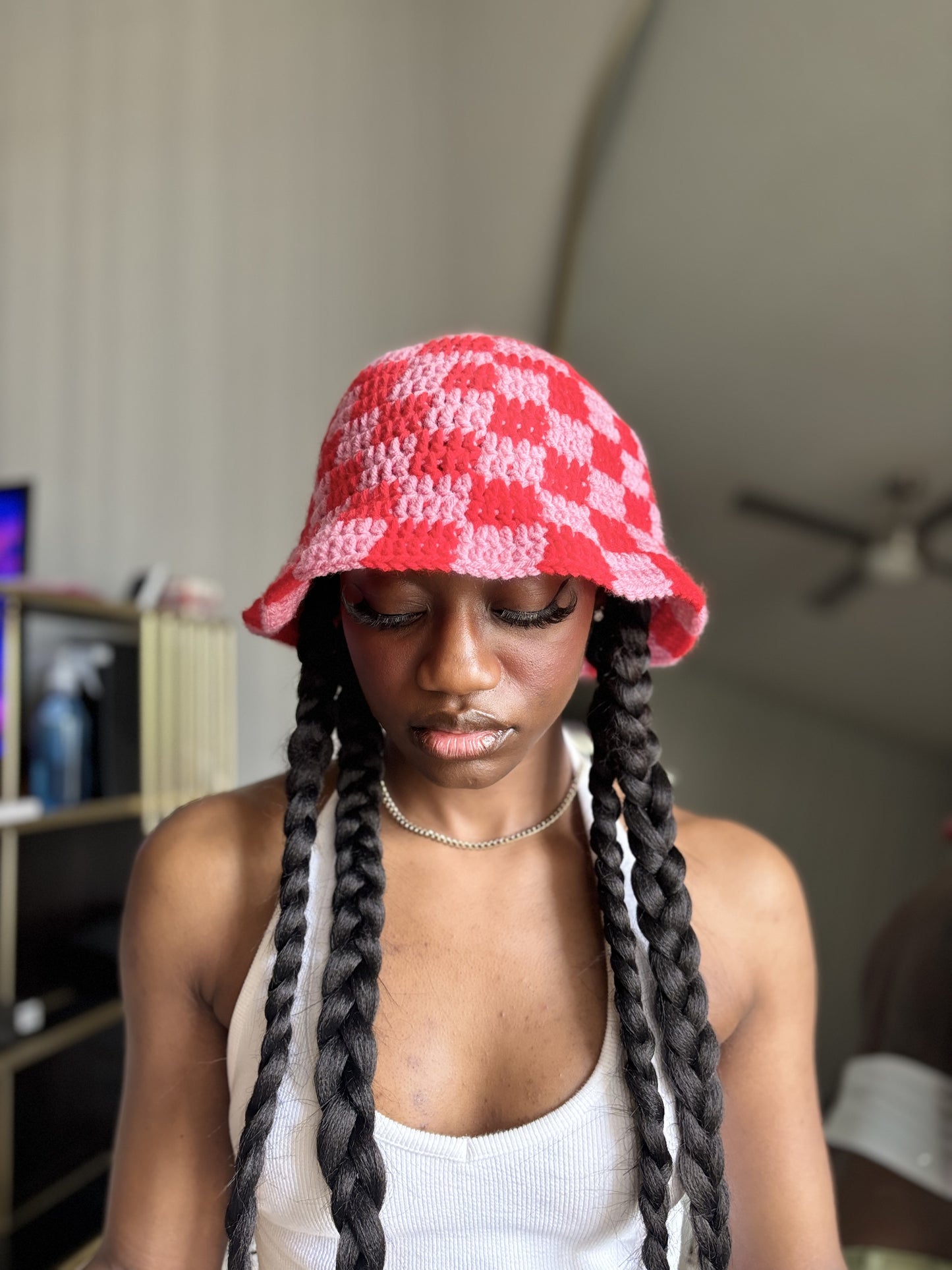 Person wearing a red and pink checkered crocheted bucket hat indoors