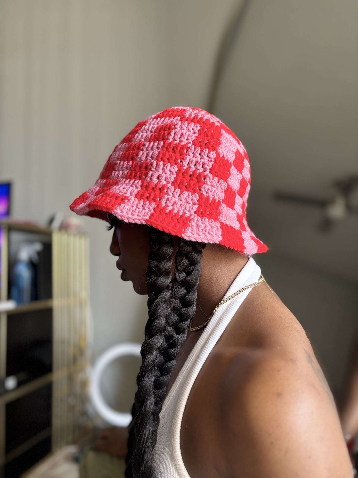 Person wearing a red and pink checkered crocheted bucket hat indoors.