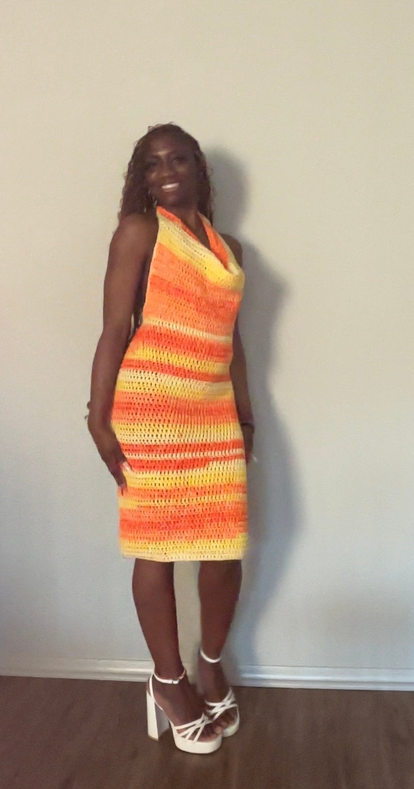 Woman wearing a colorful striped crochet dress against a plain wall.