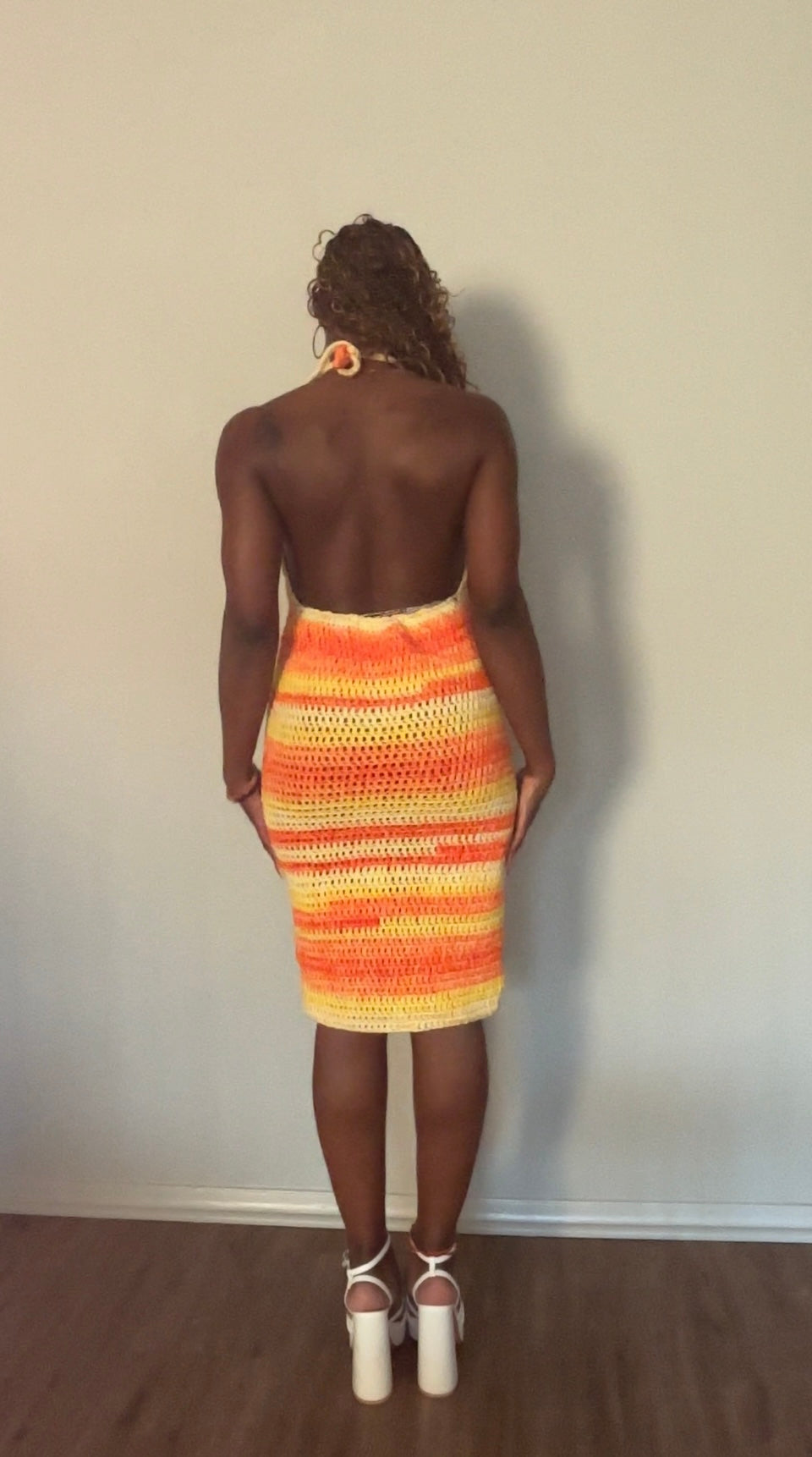 Person wearing a colorful striped crochet dress against a plain wall.