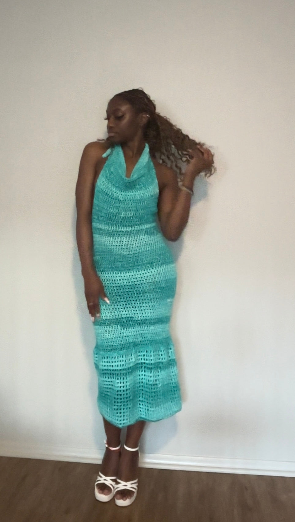 Woman wearing a teal crochet dress against a white wall