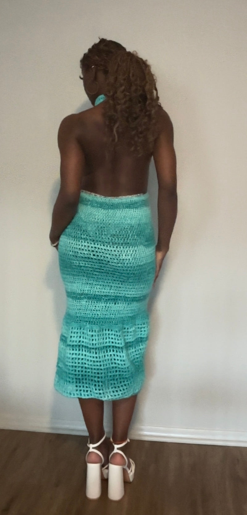 Person wearing a teal crochet dress against a plain wall.