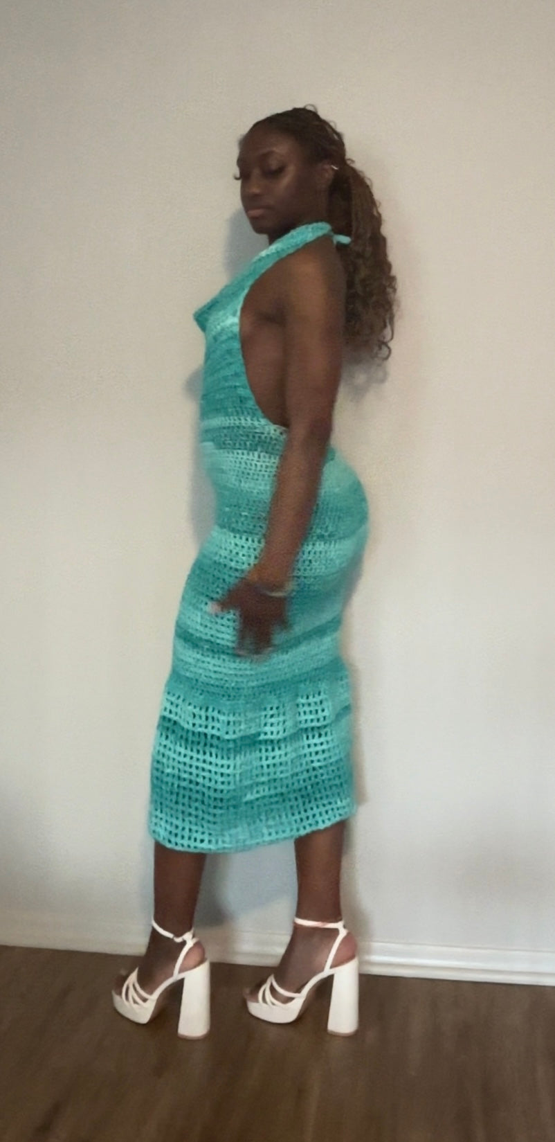 Woman wearing a teal patterned crochet dress against a white wall.
