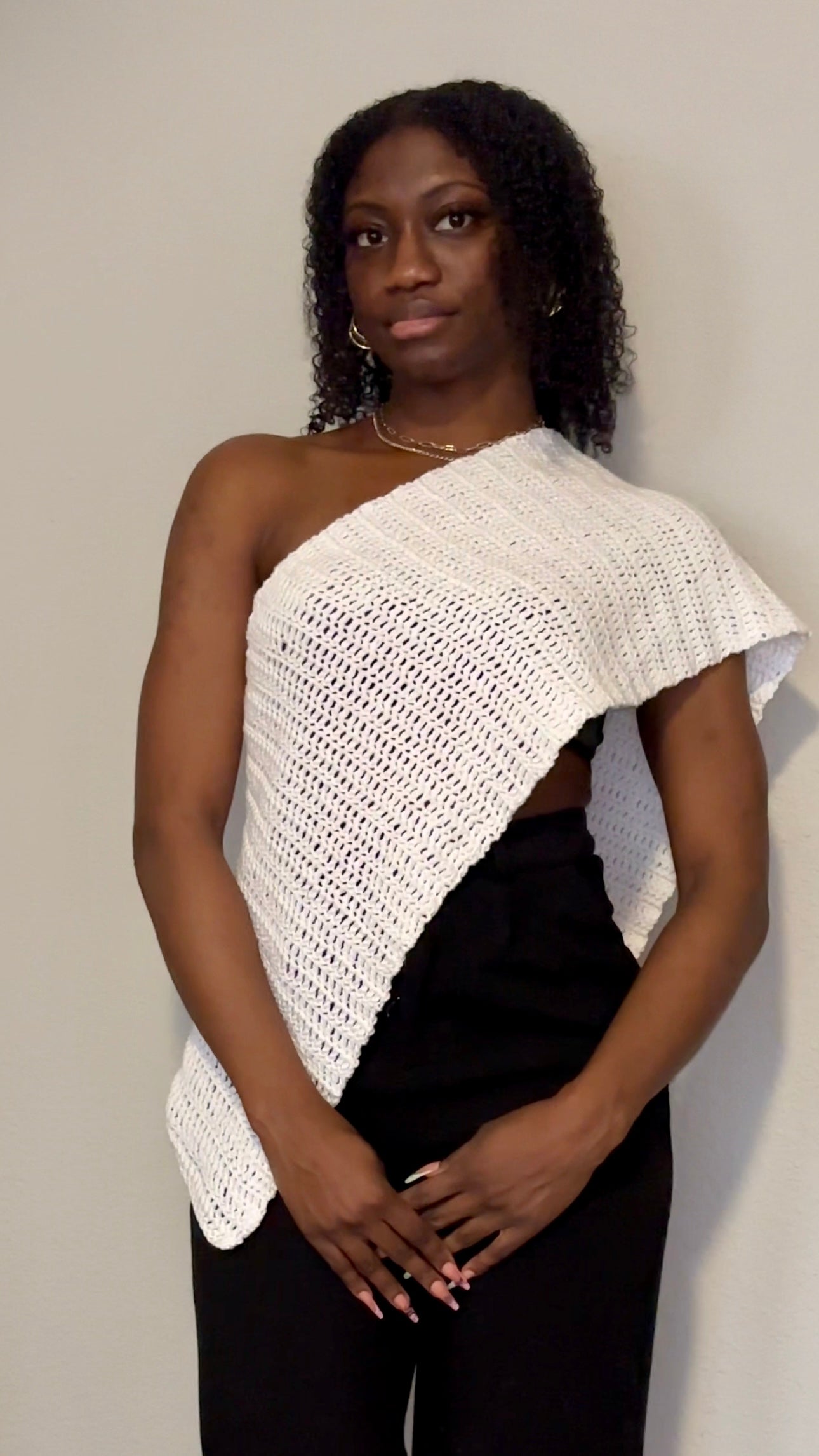 Woman wearing a white crocheted shawl over one shoulder against a plain background