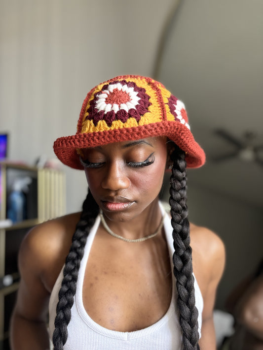 Woman wearing a colorful crocheted hat with braided hair indoors.