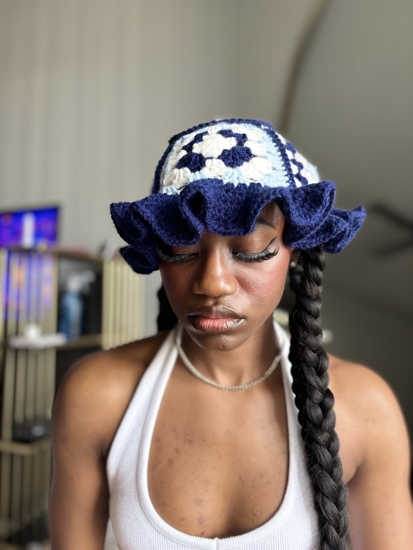 Woman wearing a blue and white patterned crocheted hat with ruffled brim indoors.