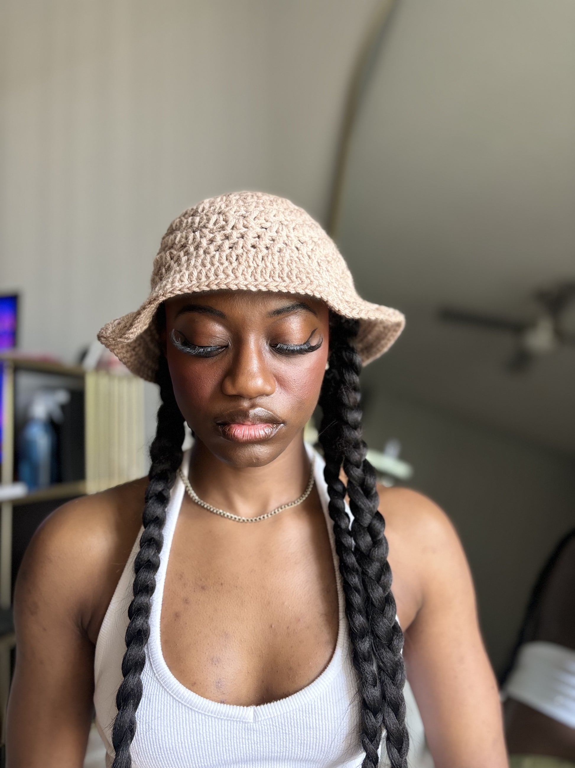 Woman wearing a beige crocheted bucket hat with braided hair indoors.