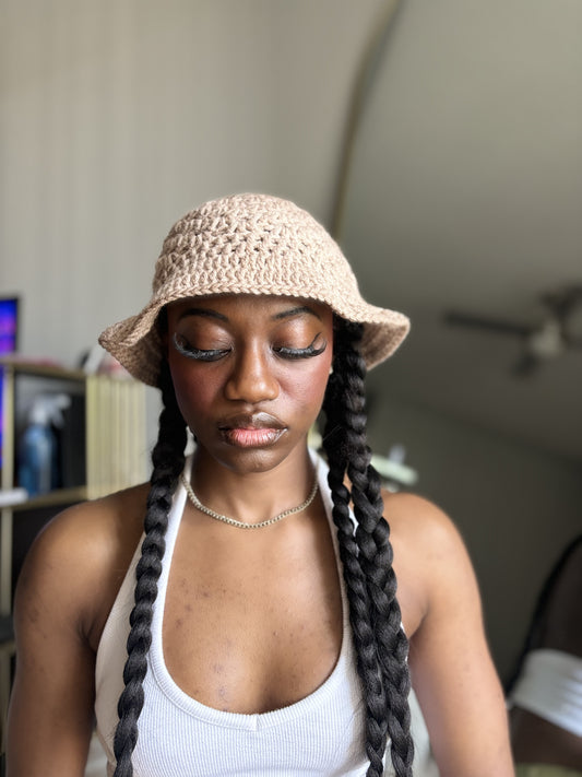Woman wearing a beige crocheted bucket hat with braided hair indoors.