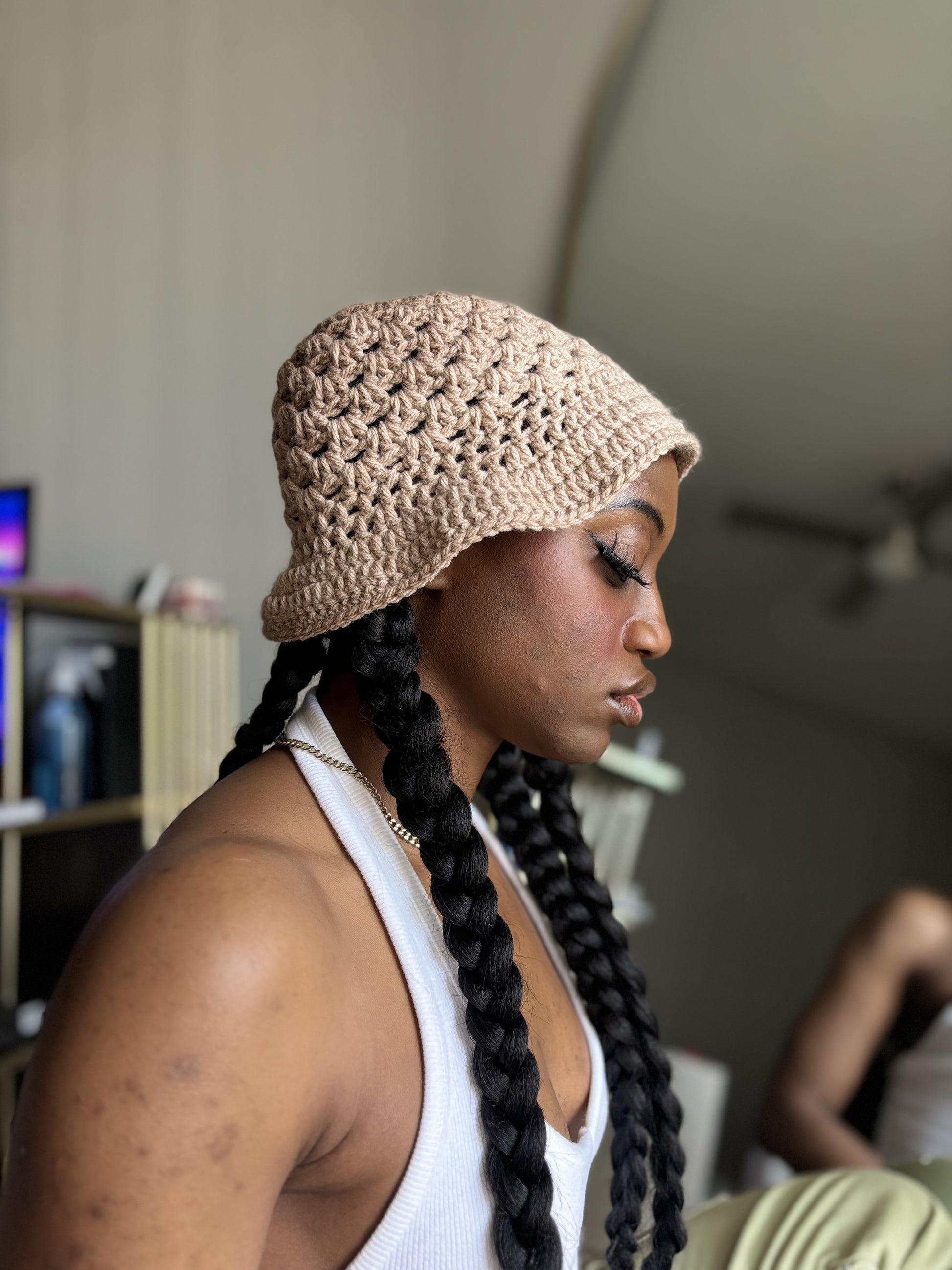 Woman wearing a beige crochet hat with braided hair indoors.