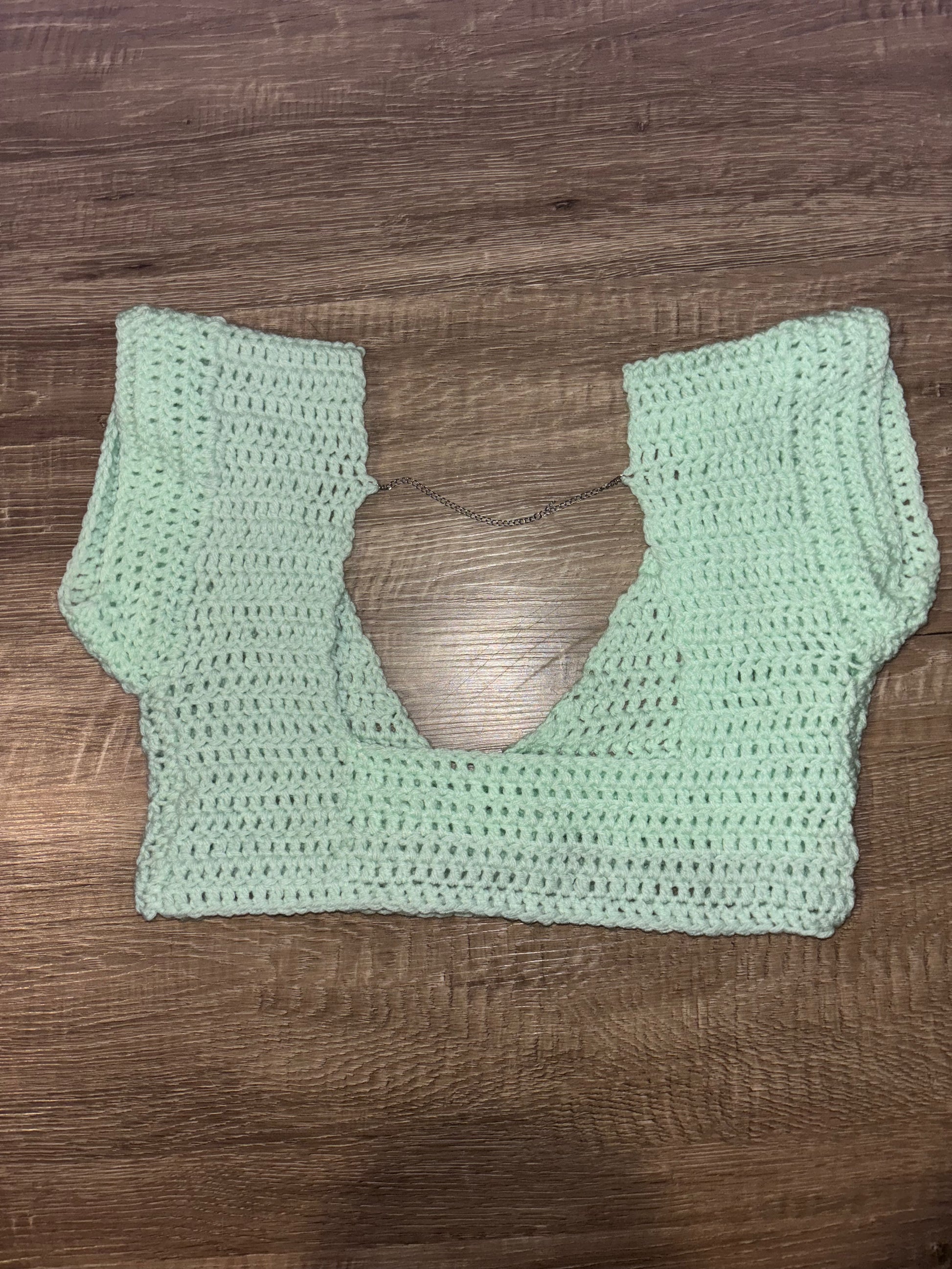 A mint green crocheted crop top with a scoop neckline and wide short sleeves, laid flat on a brown wooden surface.