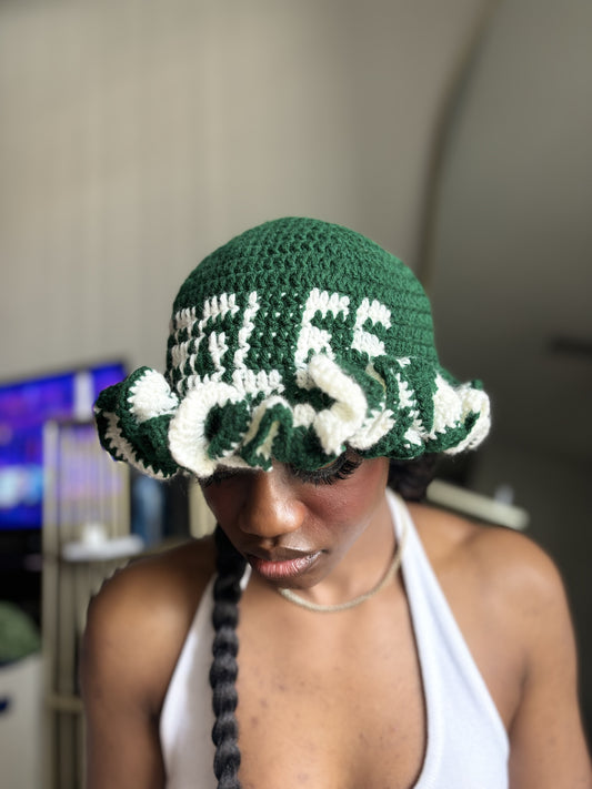 Person wearing a green and white crochet ruffle hat with text, indoors.