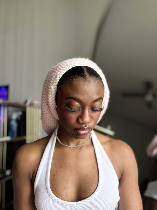Woman wearing a white tank top and pink crochet hat in a room with books and decor.