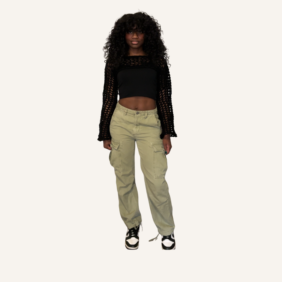 Person wearing a black crochet mesh shrug, black crop top, green cargo pants, and black and white sneakers on a white background