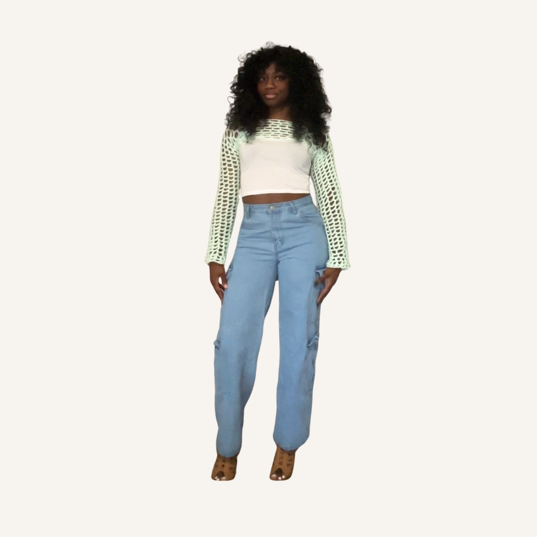 Woman wearing a white top with green crochet mesh shrug and light blue jeans on a white background
