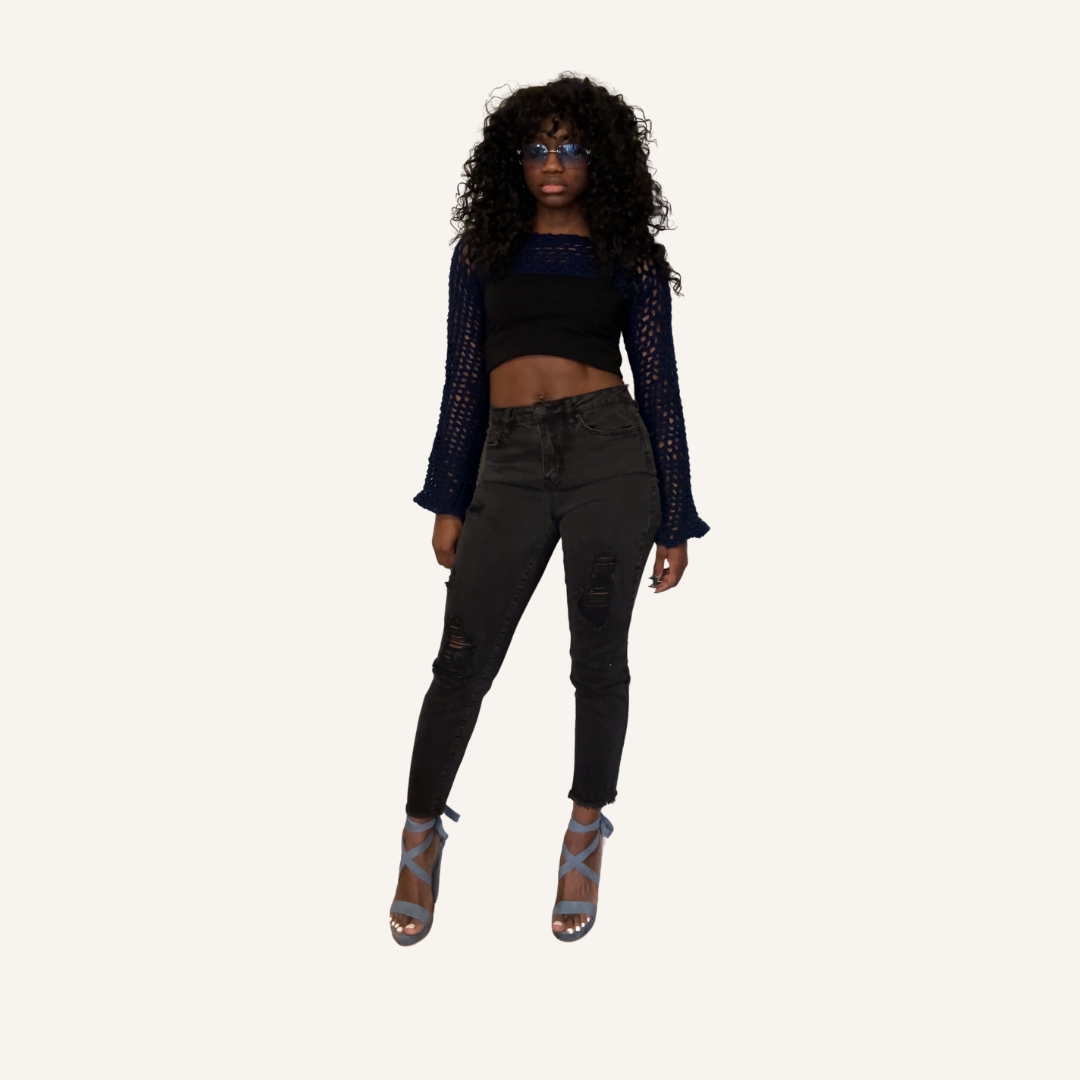 Woman wearing a navy mesh crochet shrug, black top and black jeans on a white background