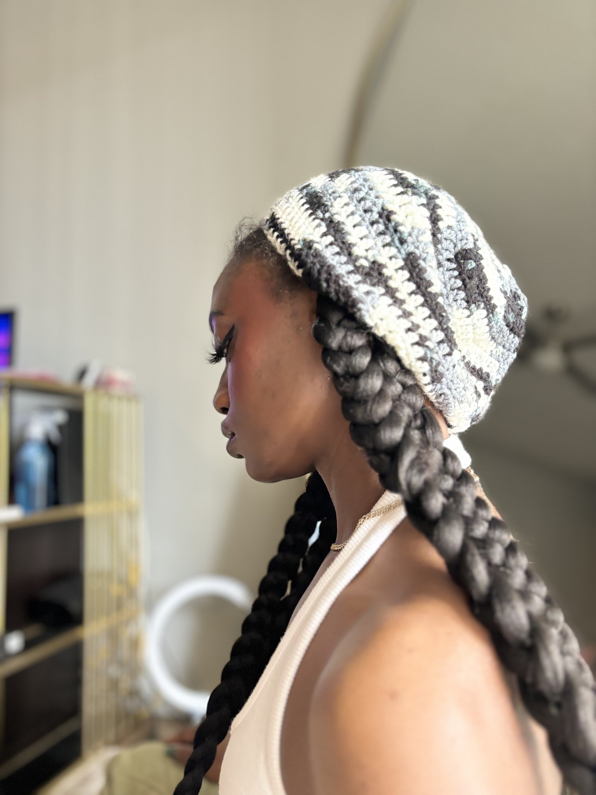 Woman with braided hair wearing a patterned crochet beret indoors.