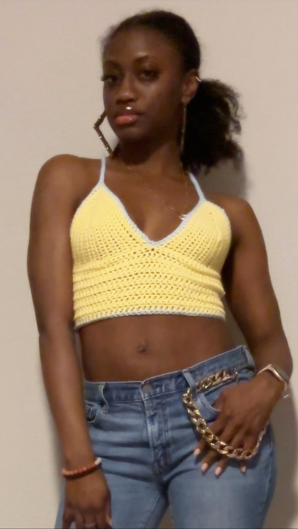 Woman wearing a yellow crochet top and blue jeans against a plain background
